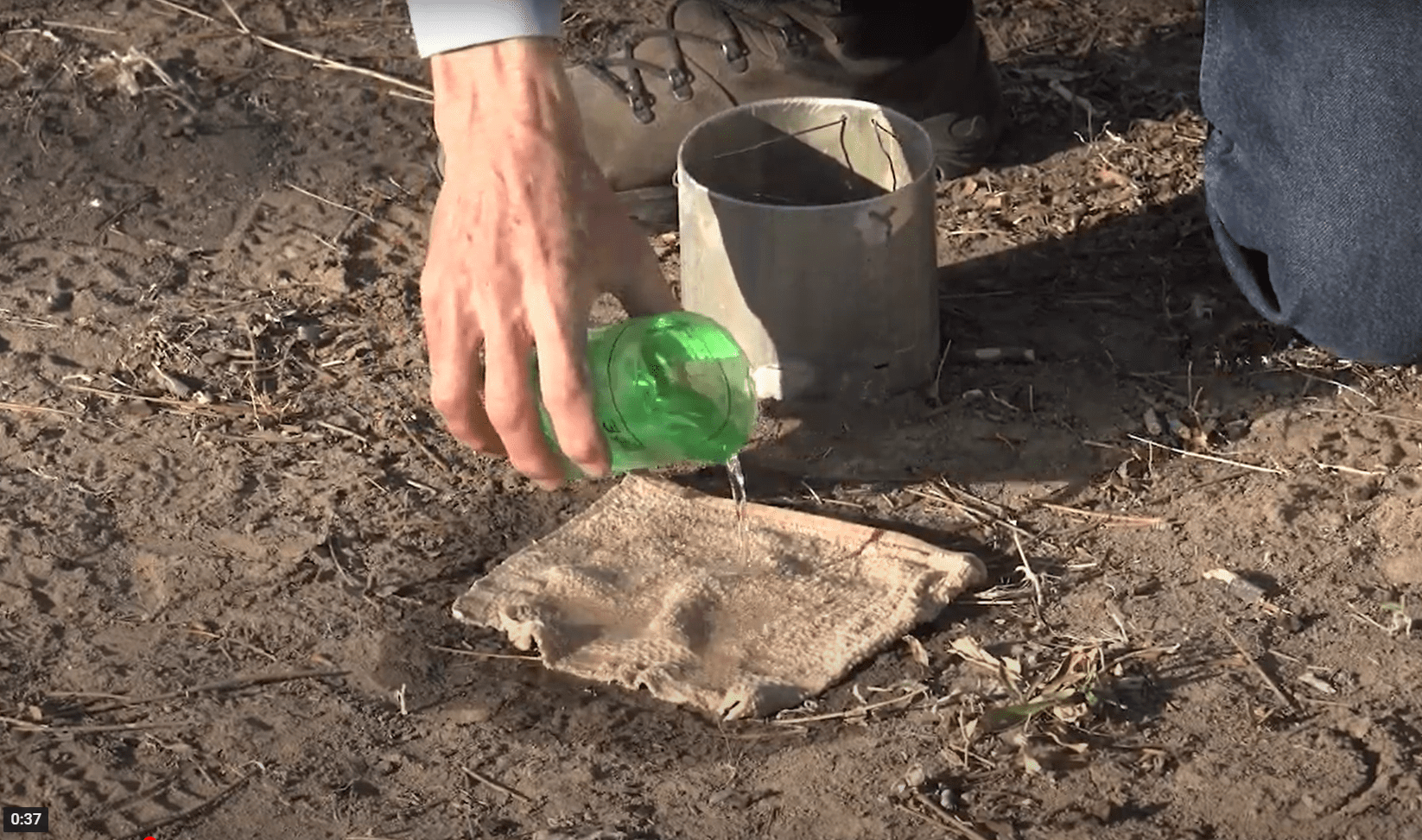 a hand pouring water on top of a cloth on soil