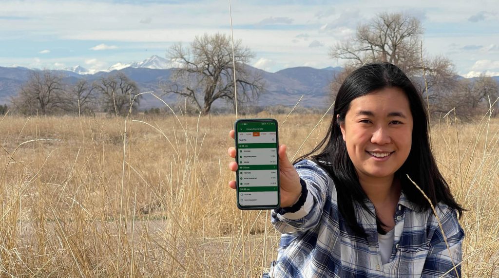 A woman showing the new LandPKS Soil ID app on her mobile phone in a rangeland.
